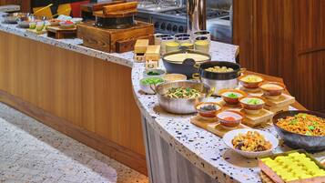 A buffet with various dishes and a pizza oven in the background.