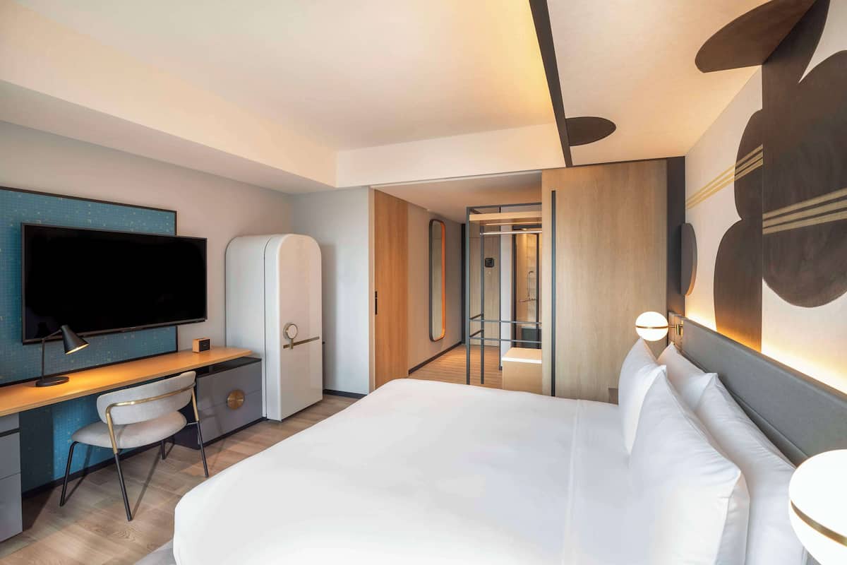 Une chambre d’hôtel moderne dotée d’un grand lit, d’un bureau avec une chaise, d’une télévision à écran plat et d’un miroir.