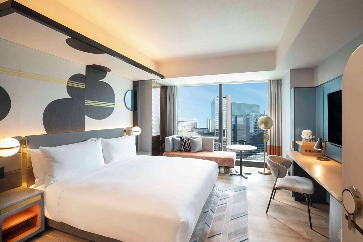 Une chambre d’hôtel moderne dotée d’un grand lit, d’un bureau, d’une chaise et offrant une vue sur le panorama urbain.