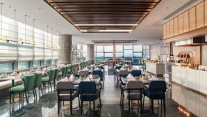 Un restaurant moderne doté d’une grande salle à manger, de hauts plafonds et de larges fenêtres offrant une vue sur la ville.