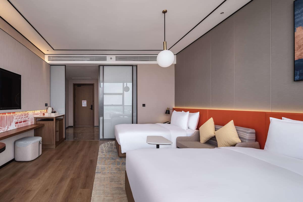 Une chambre d’hôtel moderne équipée de deux lits, d’un bureau, d’une télévision et d’une grande fenêtre.