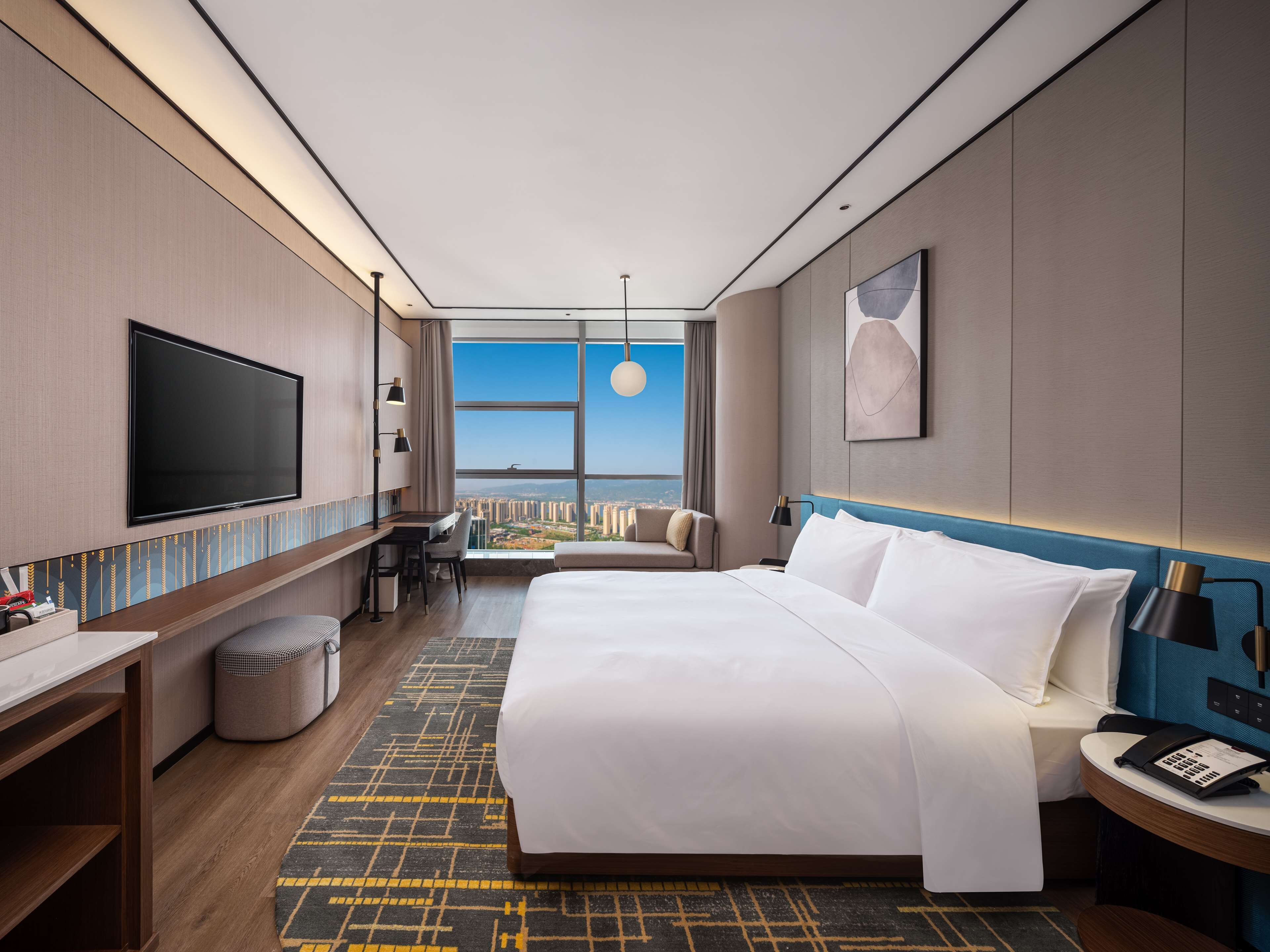 Ein Hotelzimmer mit einem großen Bett, einem Schreibtisch, einem Fernseher und Blick auf die Stadt.