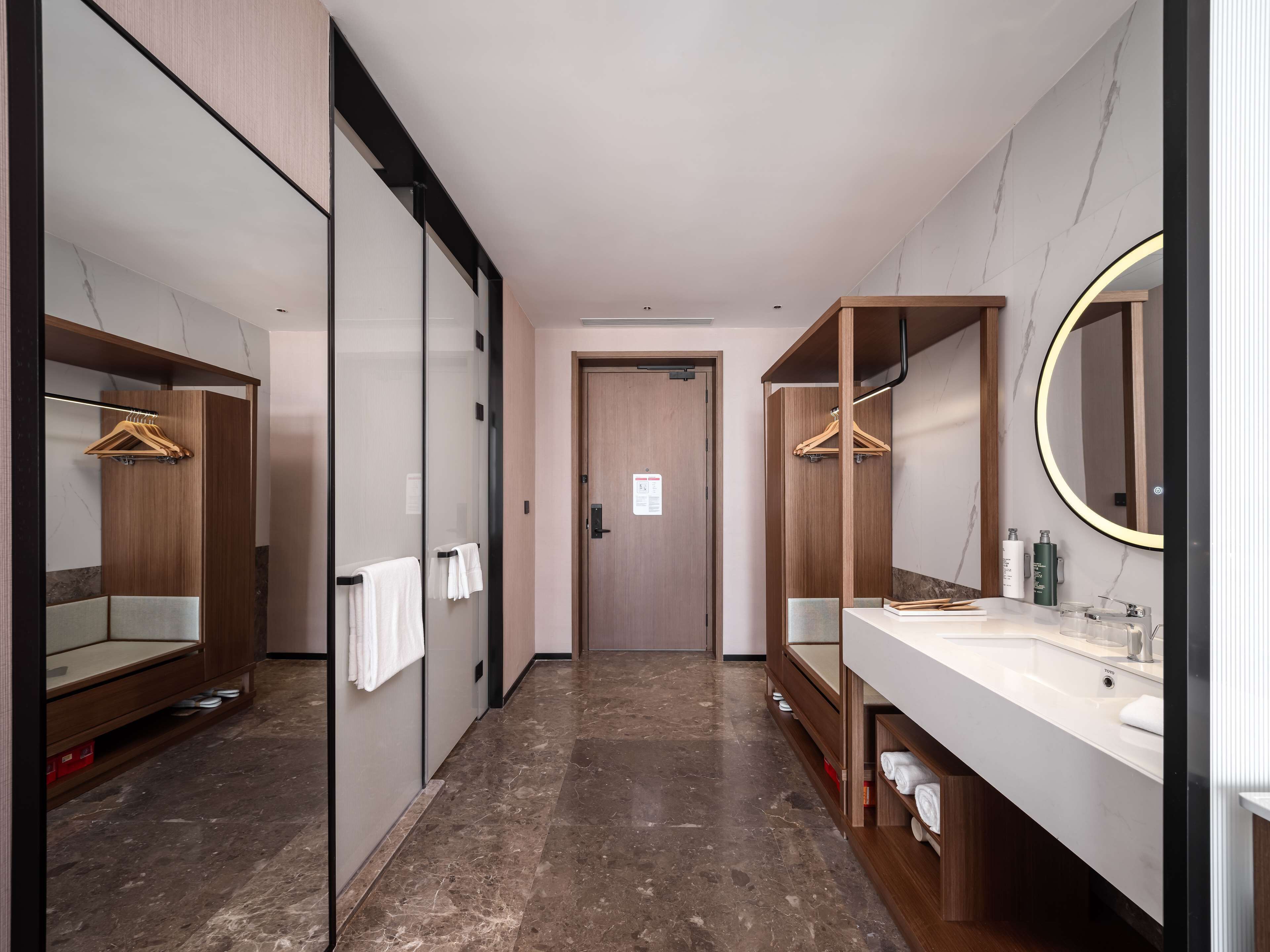 A modern hotel bathroom with a marble floor, wooden cabinets, and a large mirror.