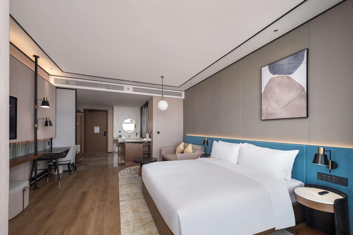 Une chambre d’hôtel moderne avec un grand lit, un bureau, une chaise, une petite table et une table de chevet.
