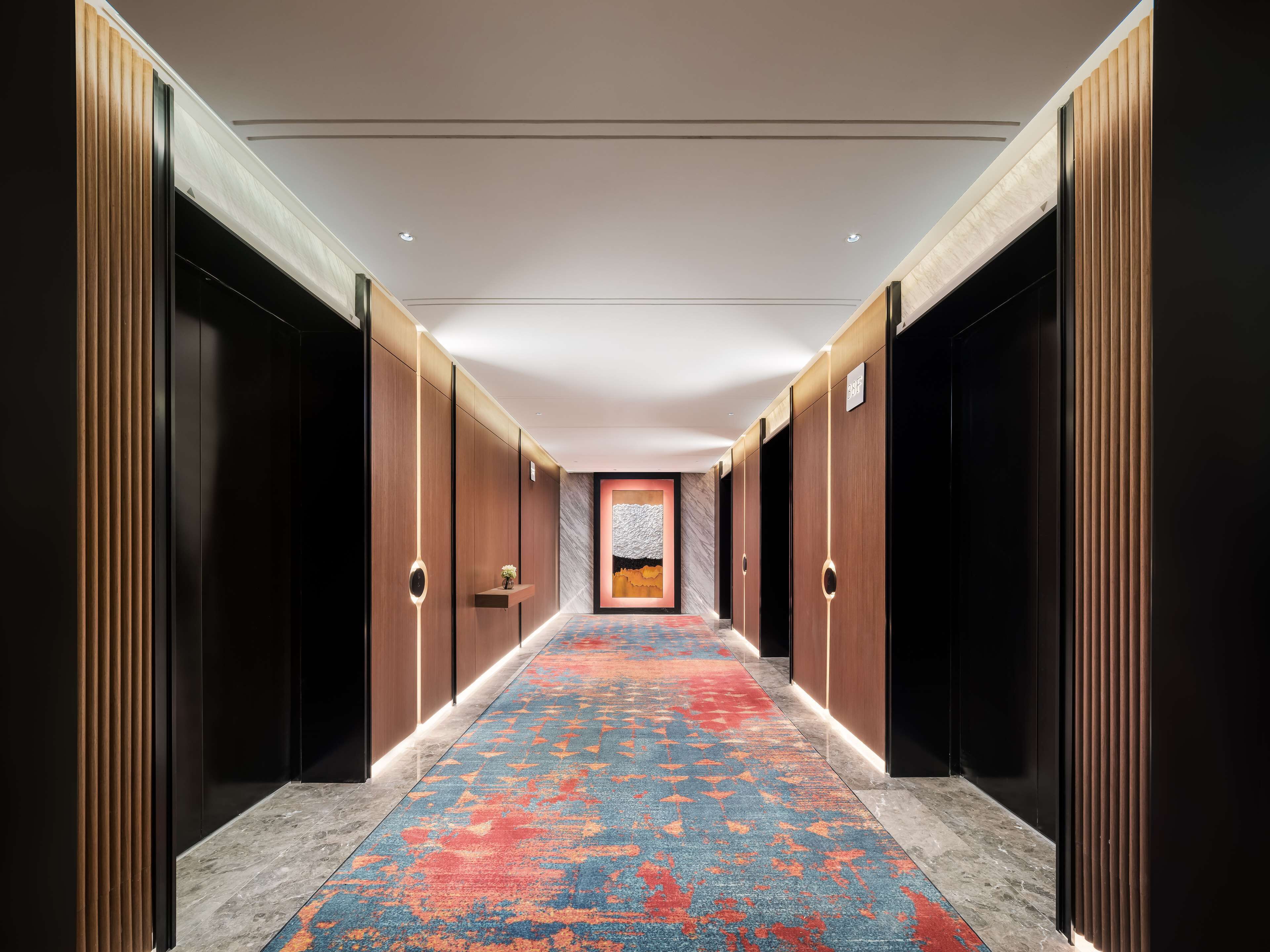 Un pasillo moderno de hotel con alfombra estampada, paneles de madera y una pared de mármol con un cuadro.