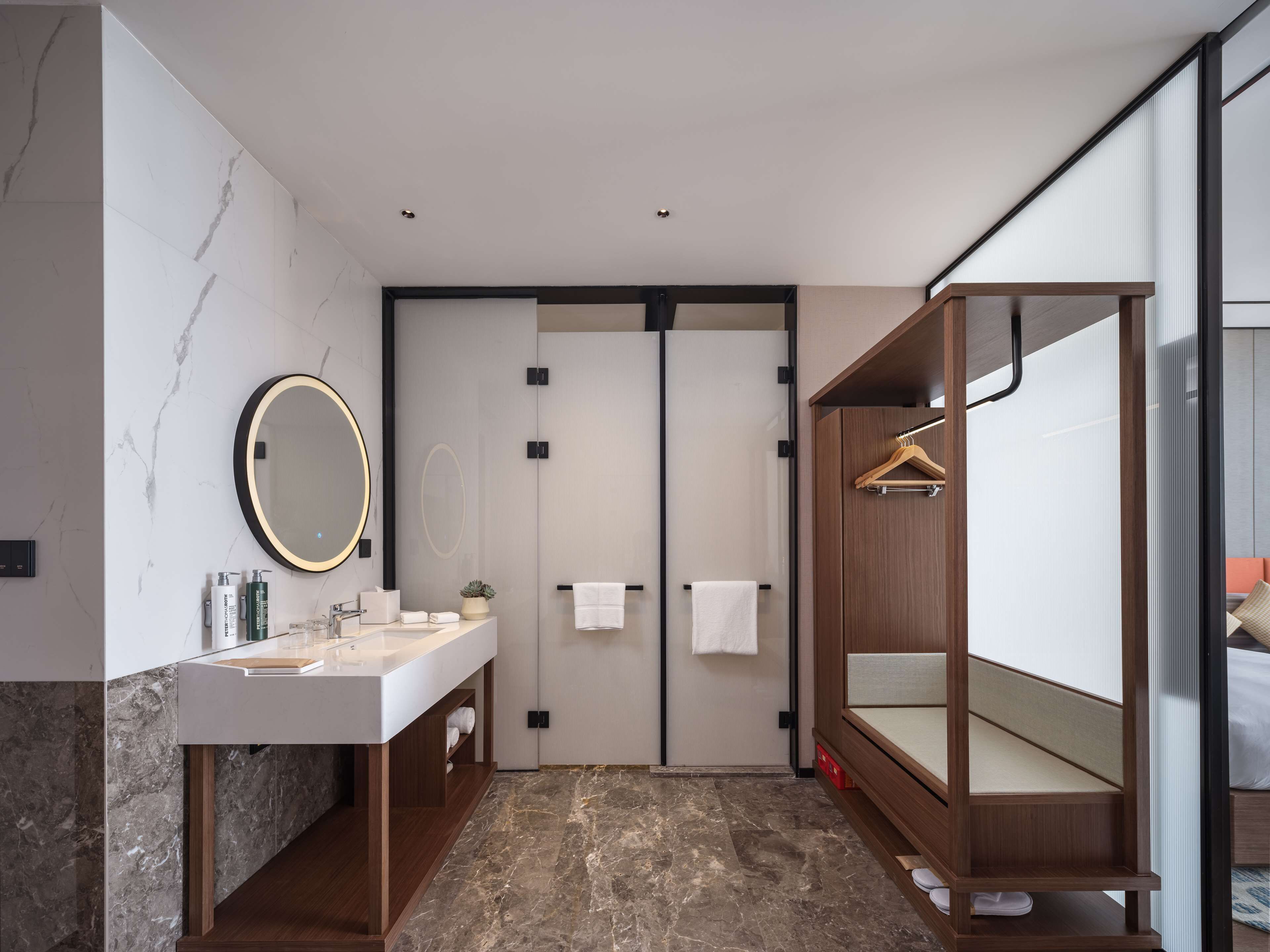 A modern bathroom with a marble floor, a large mirror, a vanity with a sink, and a wooden wardrobe.