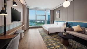 Une chambre d’hôtel moderne, dotée d’un grand lit, d’un canapé, d’une télévision et offrant une vue sur le paysage urbain.
