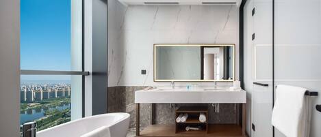 A modern bathroom with a large bathtub, a vanity with a mirror, and a view of a cityscape through a large window.
