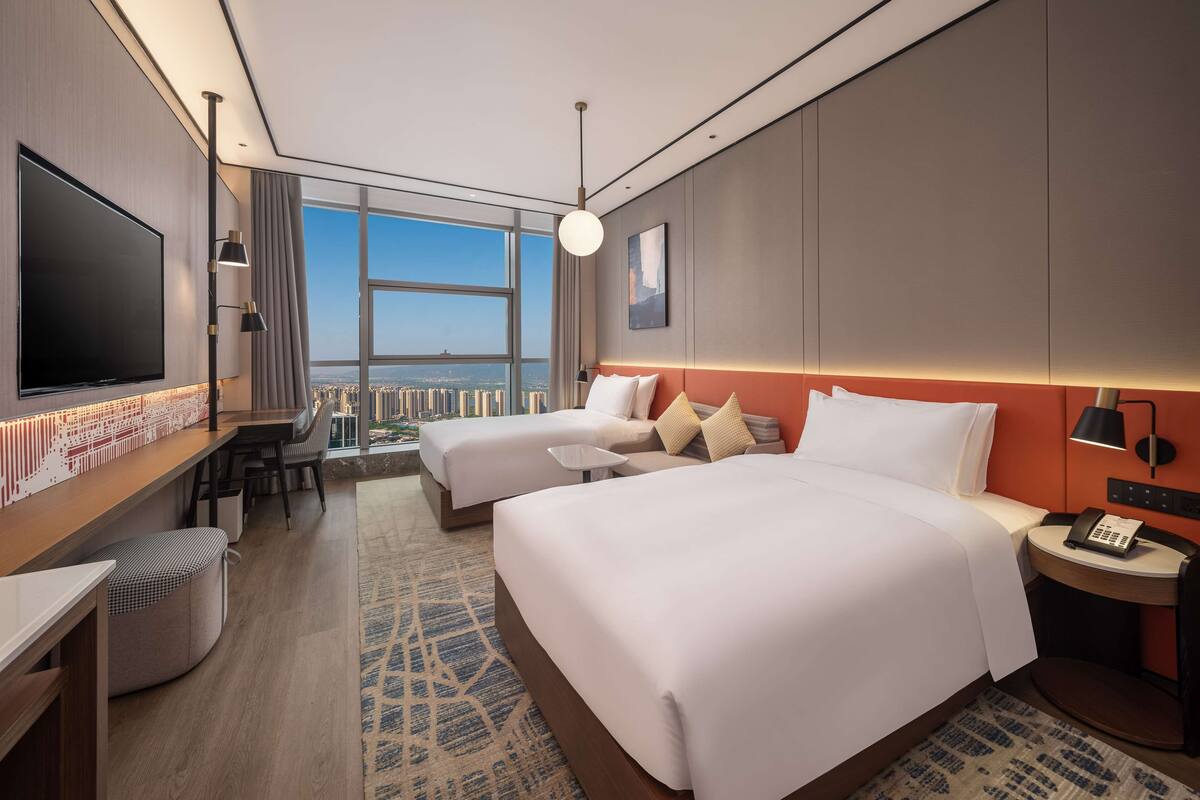 Une chambre d’hôtel moderne avec deux lits, une télévision, un bureau et une vue sur la ville.