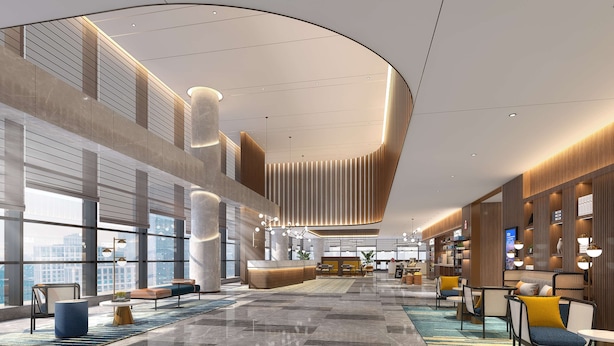 Un hall d’entrée spacieux avec de hauts plafonds, de grandes fenêtres offrant une vue sur la ville, un espace salon central et des luminaires modernes.