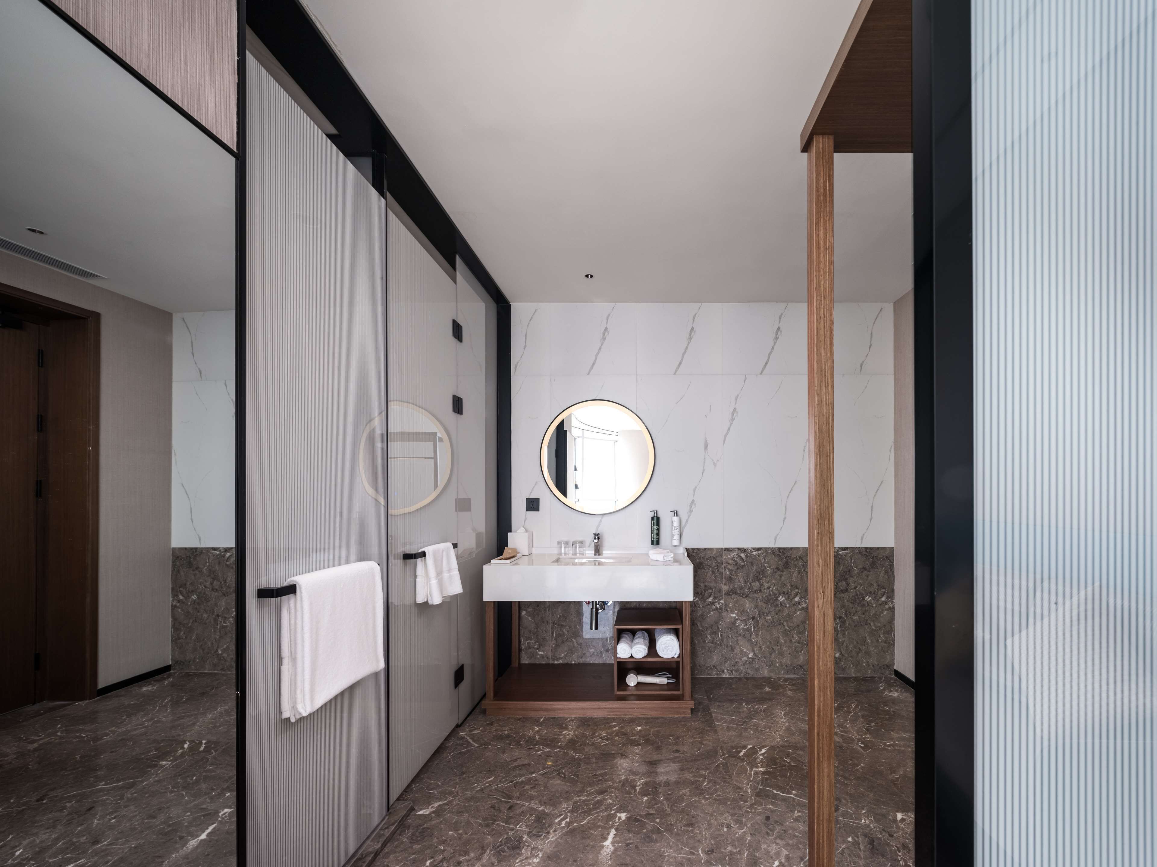 A modern bathroom with a marble floor, a white sink with a mirror, and a wooden door.
