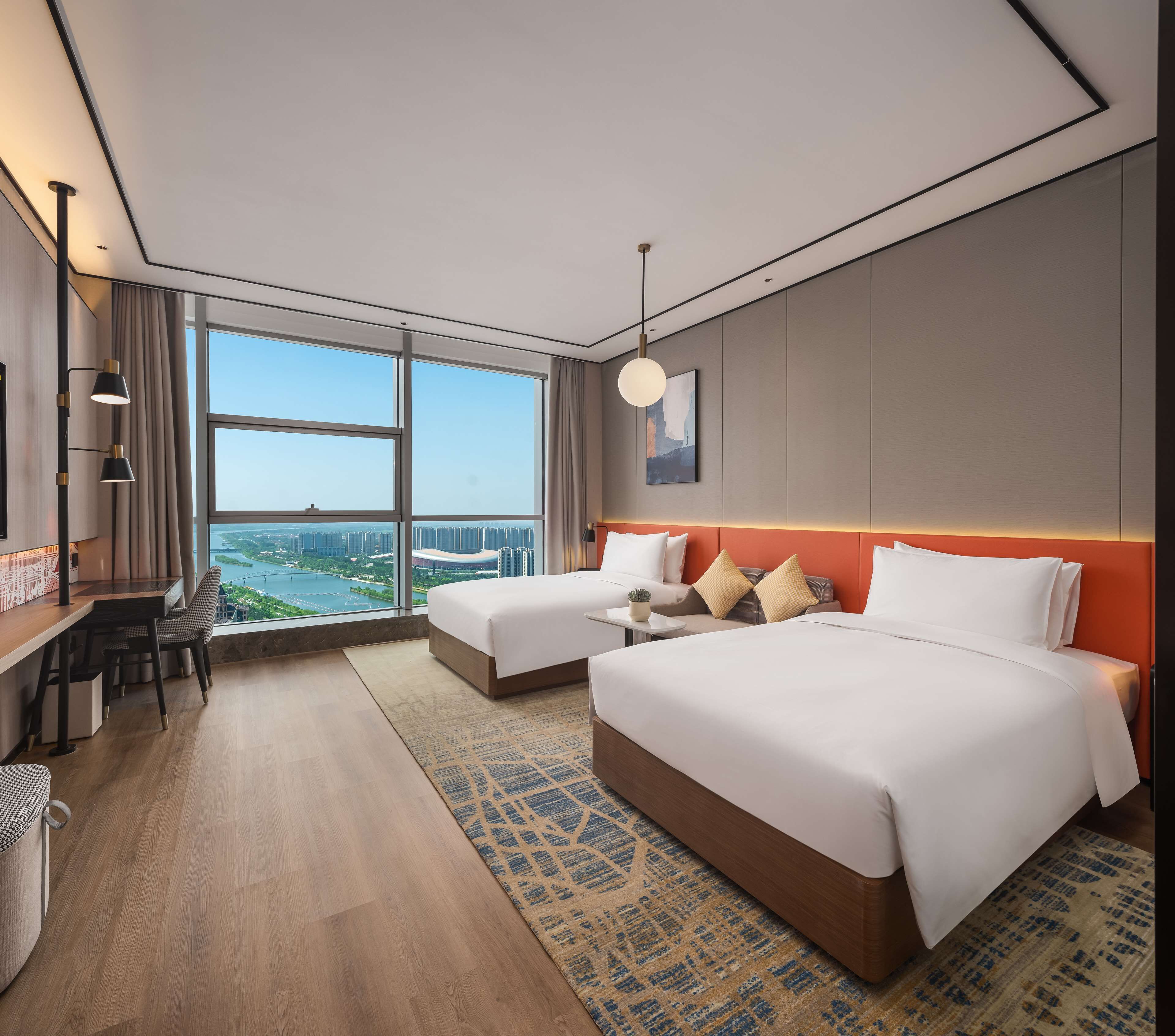 Een moderne hotelkamer met twee bedden, een bureau en een groot raam met uitzicht op de stad.
