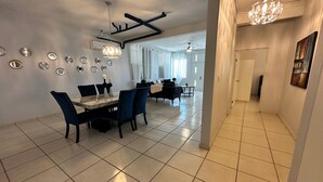 A spacious dining area with a marble table and blue upholstered chairs, a chandelier, and decorative wall mirrors.