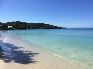 Una spiaggia con acque cristalline turchesi, un litorale sabbioso e un’isola boscosa sullo sfondo.