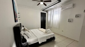 A bedroom with a bed, a ceiling fan, a window with curtains, and a wall-mounted air conditioner.