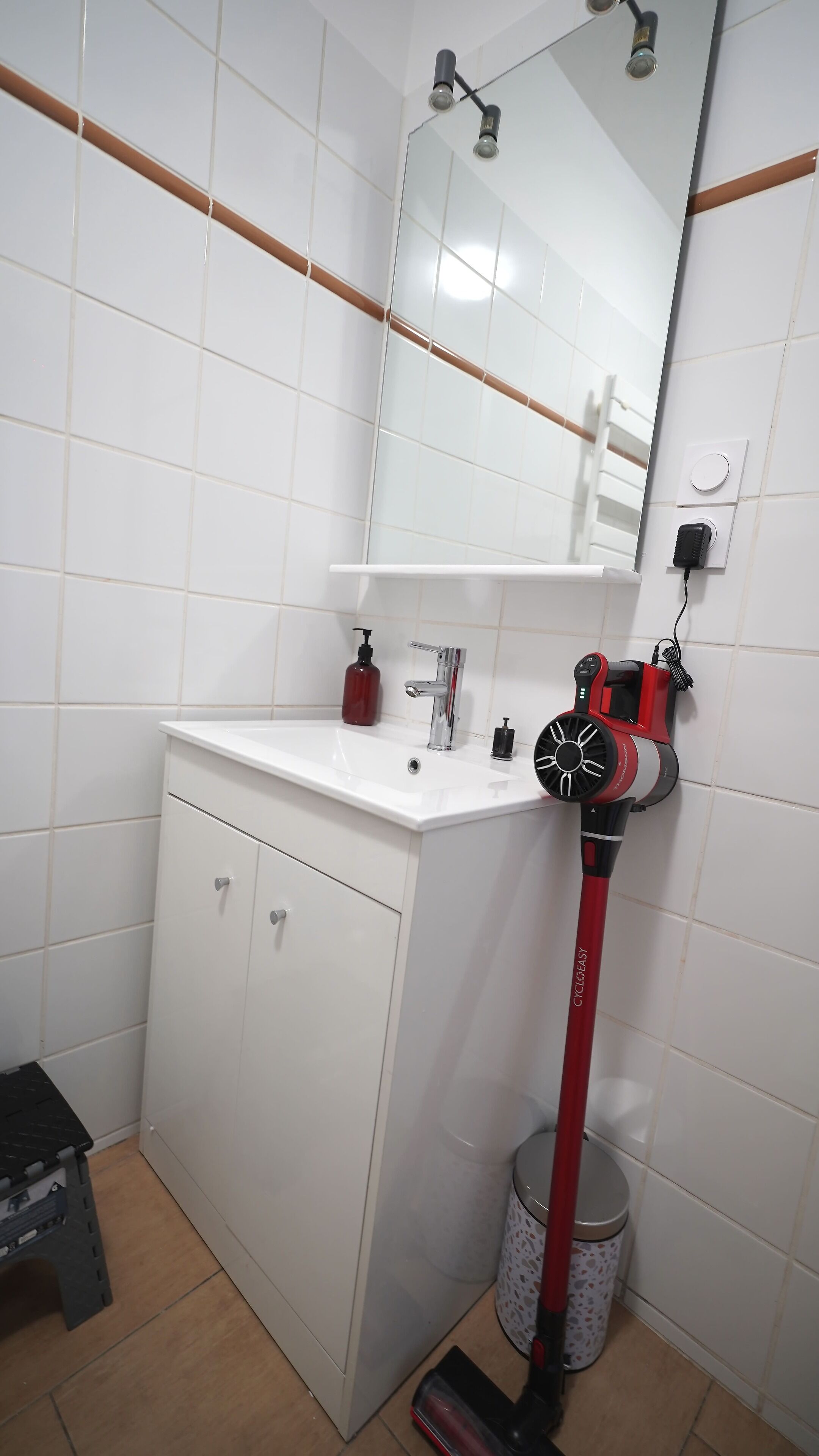 A bathroom with a white sink, mirror, and a red vacuum cleaner.