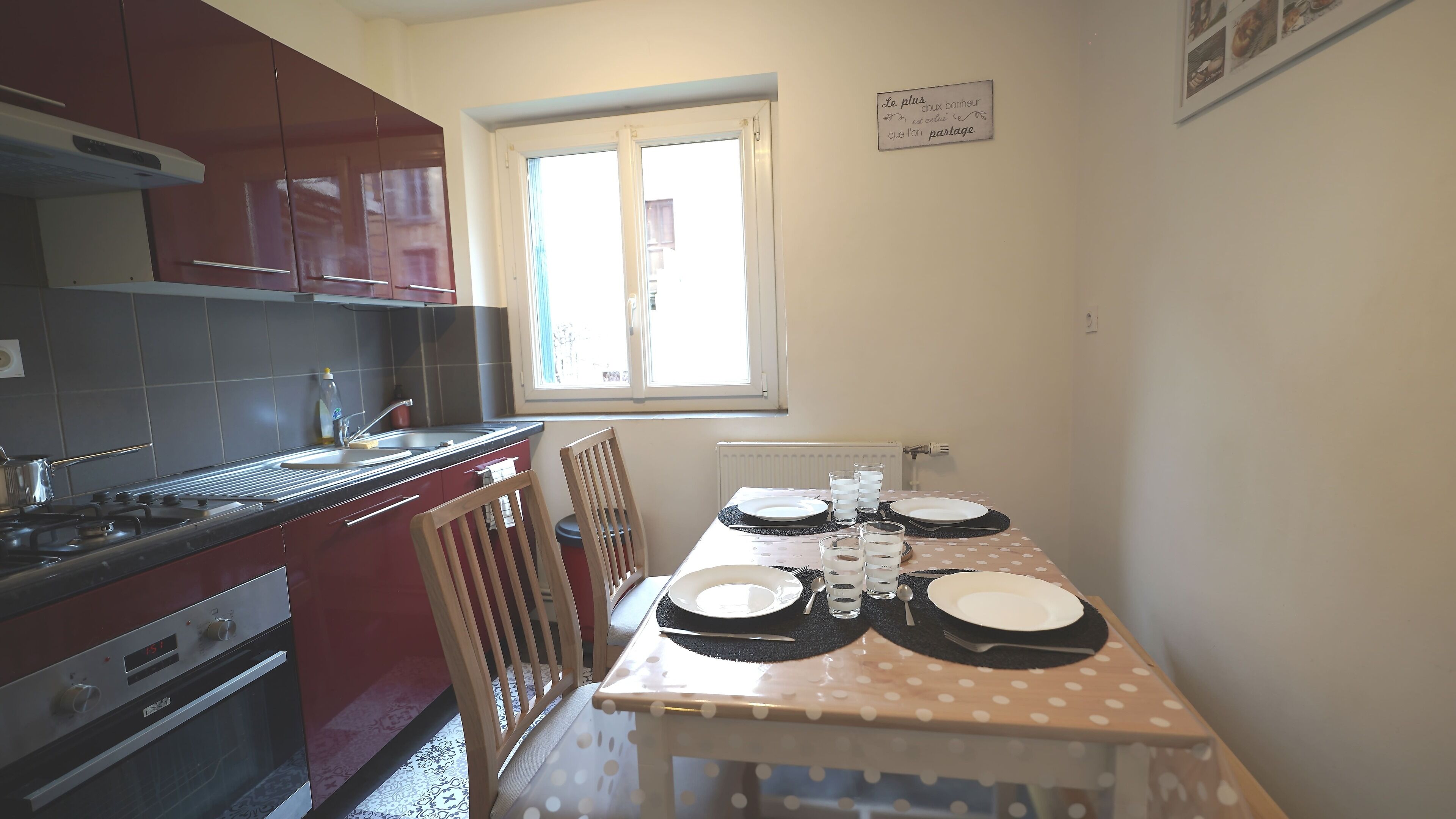 A compact kitchen with a dining table set for two, equipped with plates, glasses, and cutlery.
