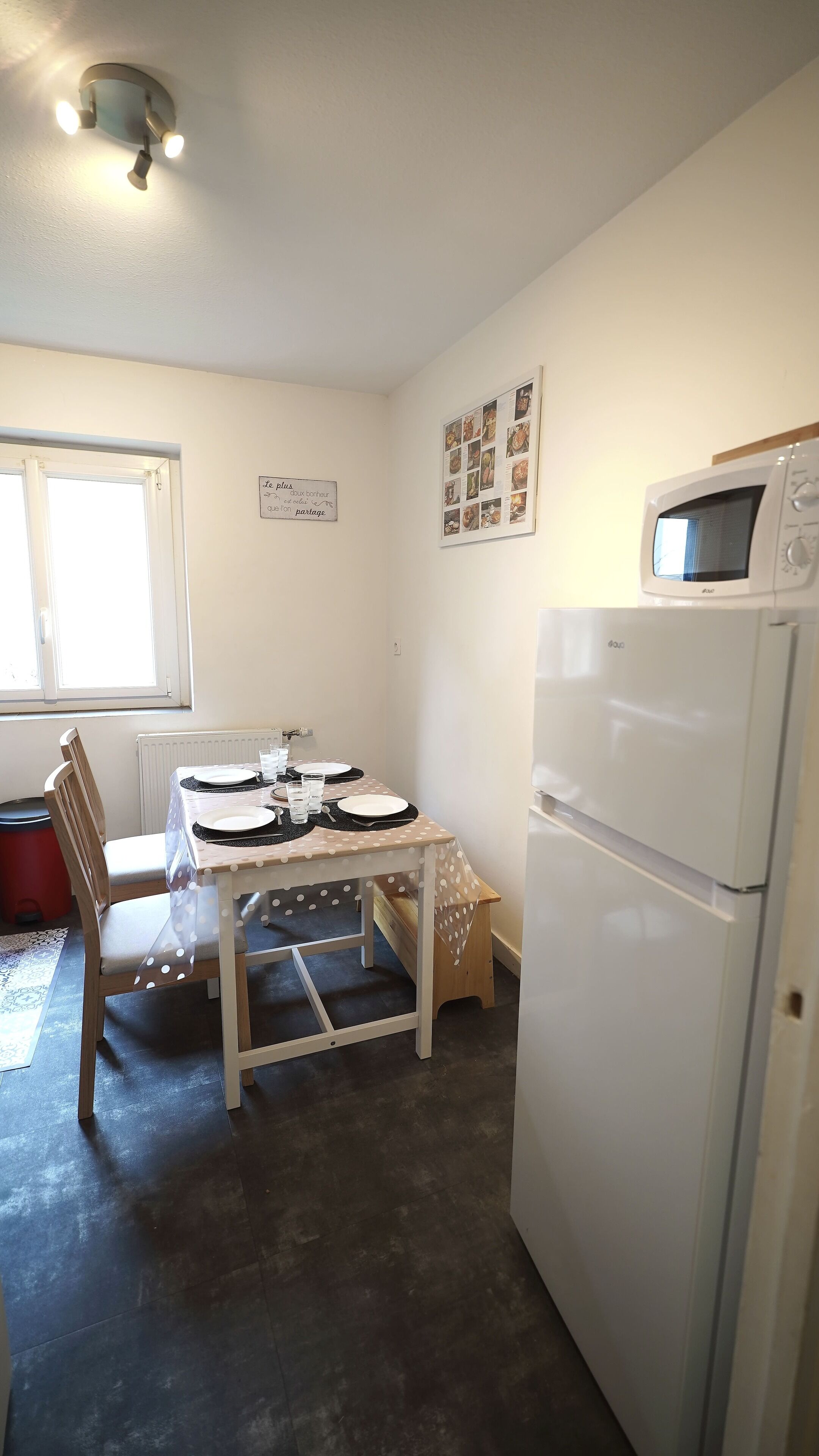 A compact kitchen with a dining table set for four, a refrigerator, and a wall-mounted microwave.