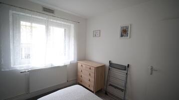 A room with a radiator, a wooden dresser, a metal rack, and two framed pictures on the wall.