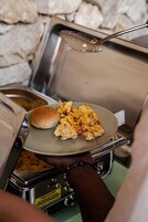 Una barra de desayuno con huevos revueltos, salchicha y un panecillo en un plato.