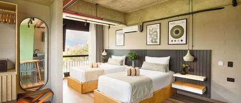 A modern hotel room with two beds, a dining table, and a balcony with a view.