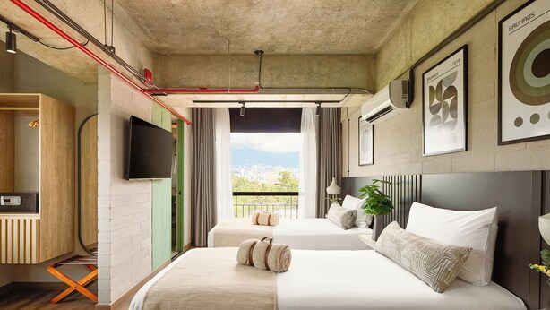 A hotel room with two beds, a TV, a balcony with a city view, and artwork on the walls. - Urbit Social Lofts (Medellín)