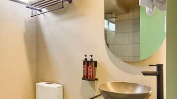Un baño moderno con inodoro, un lavamanos con recipiente amplio, toallero, espejo y extintor.