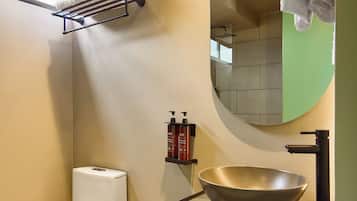 Een moderne badkamer met een toilet, een wastafel met een brede kom, een spiegel en een handdoekrek.