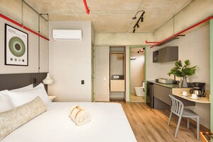Ett modernt hotellrum med en säng, ett skrivbord, en stol, ett litet pentry och ett badrum.