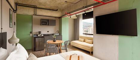 A hotel room with a bed, a sofa, a TV, a kitchenette, and a dining area.