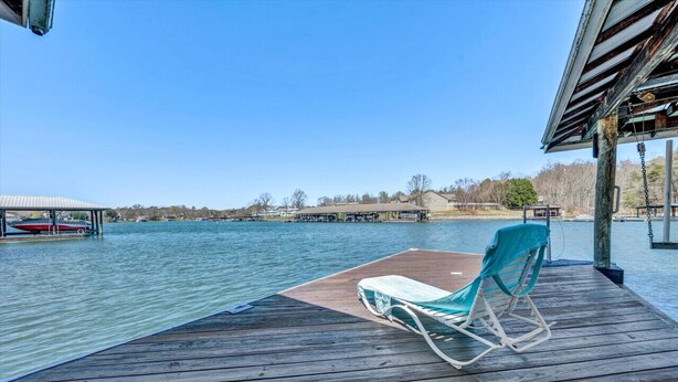 A wooden deck with a single lounge chair and a table, overlooking a calm body of water with boats and a distant shoreline. - Castaway - Family-friendly with a dog in protected cove (Huddleston)