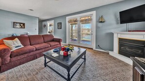 A living room with a red sofa, a coffee table with children's toys, a fireplace, and a TV mounted on the wall. - Castaway - Family-friendly with a dog in protected cove (Huddleston)