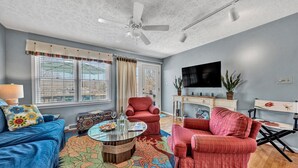 A living room with a blue sofa, red armchairs, a coffee table, and a TV on the wall. - Castaway - Family-friendly with a dog in protected cove (Huddleston)