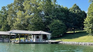 A lakeside cabin with a covered dock, surrounded by trees and a grassy area. - Castaway - Family-friendly with a dog in protected cove (Huddleston)