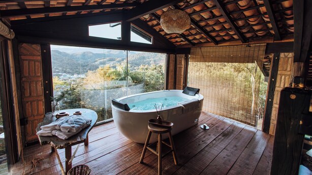 Una terraza de madera con un jacuzzi, una mesa con toallas y vistas a las montañas.