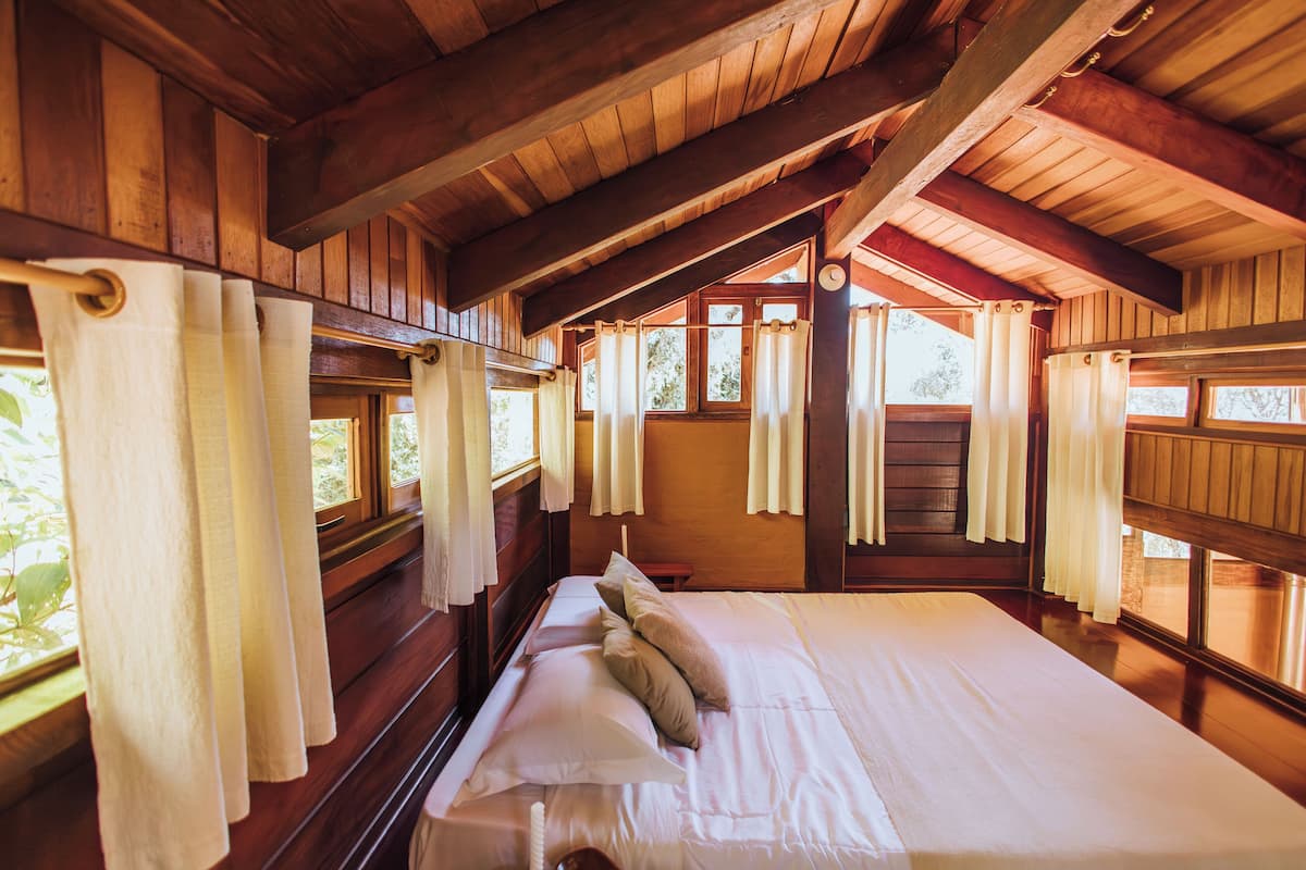 Une chambre dans une cabane en bois, avec un grand lit, des rideaux et des fenêtres.