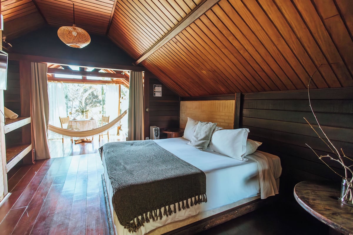 Une chambre confortable avec un plafond en bois, un lit recouvert de draps blancs, une petite table et un hamac.
