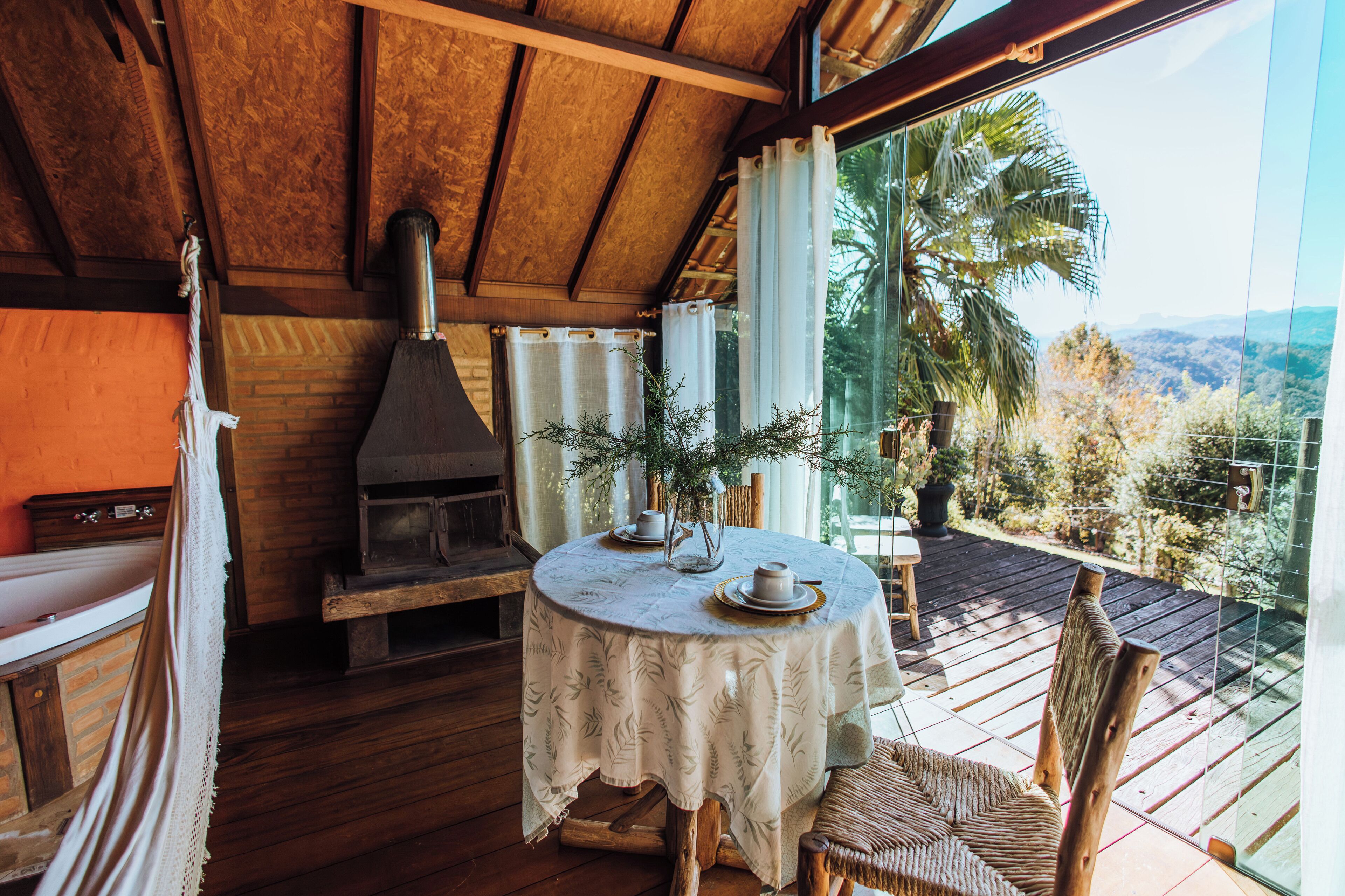 A wooden interior with a round table set for dining, a fireplace, and a view of the outdoors.