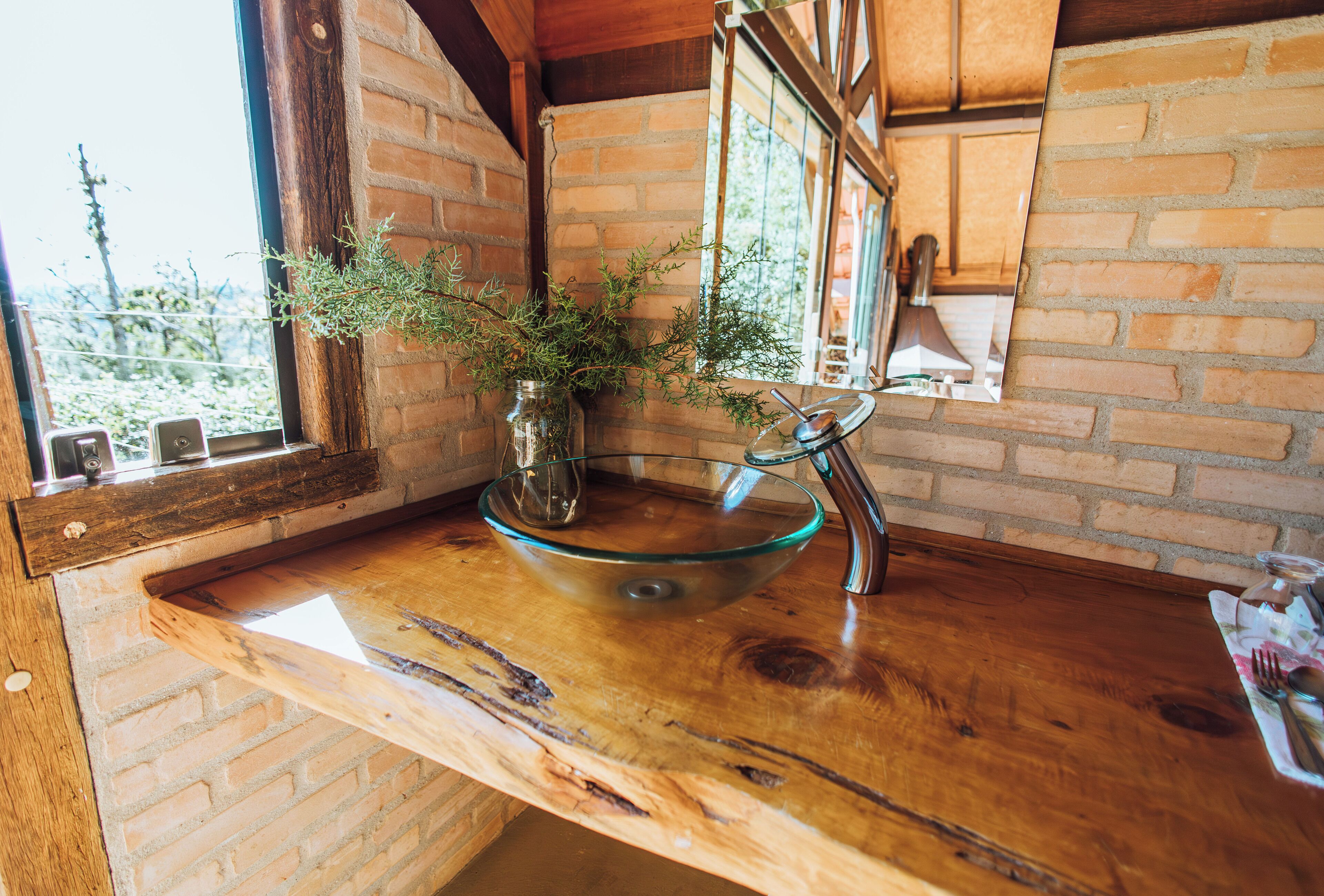 A rustic kitchen with a wooden countertop, a glass bowl sink, and a window with a view of greenery.