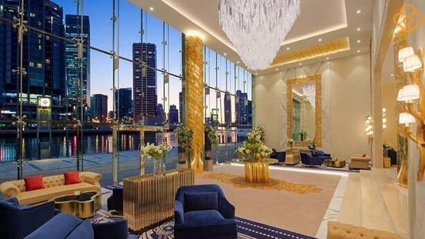 A luxurious hotel lobby with a city view, elegant furniture, and a chandelier. - Vogue | DAMAC Maison Privé | Near Dubai Mall (Dubai)