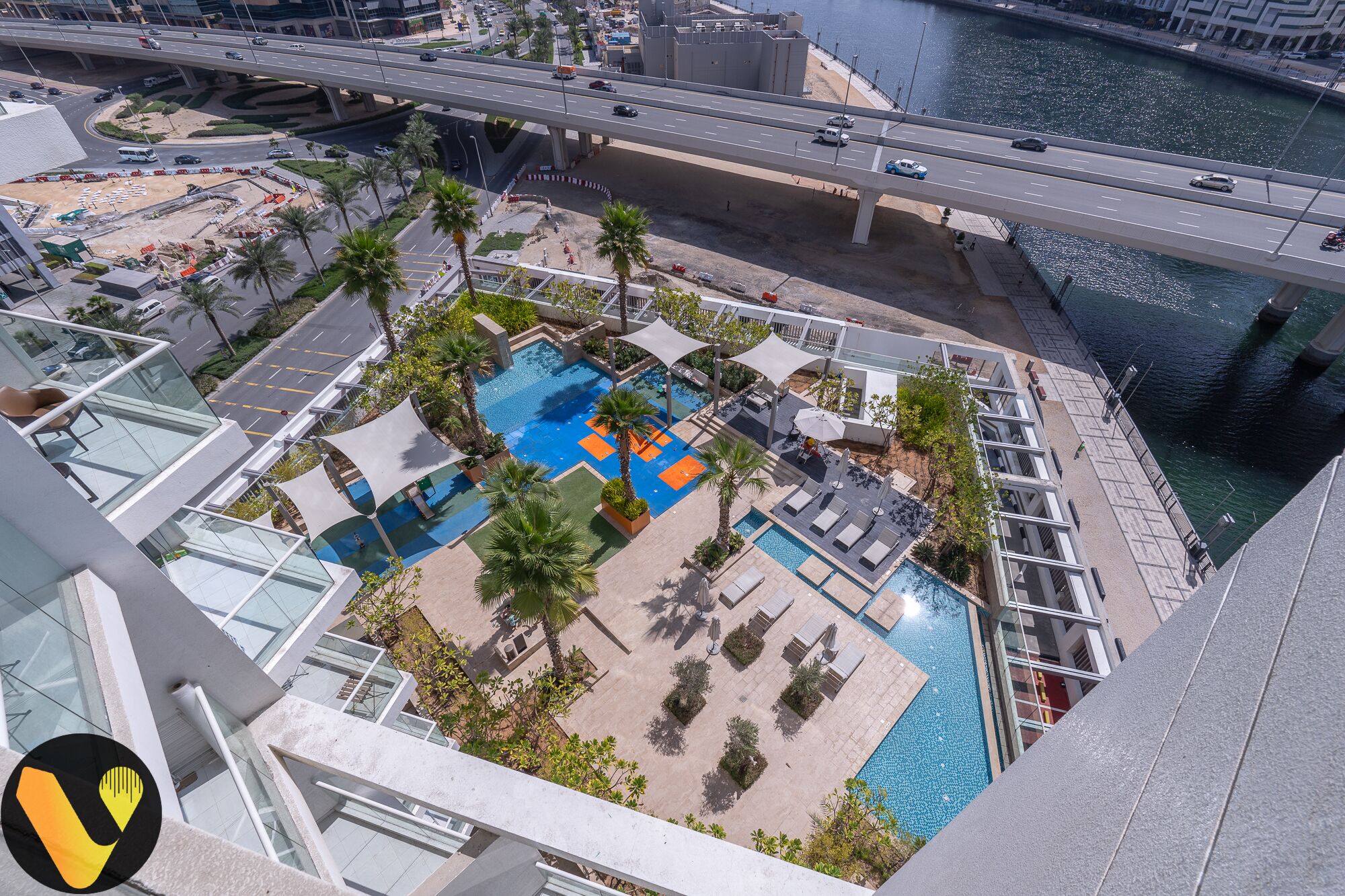 A rooftop pool area with multiple swimming pools, palm trees, and lounge chairs.