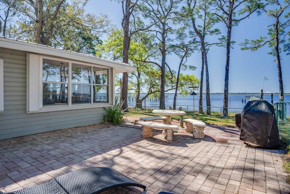 A patio with a table and chairs, a grill, and a view of the water.