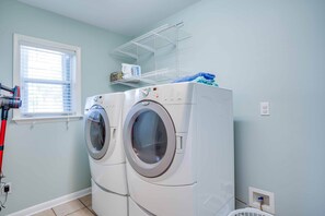 A laundry room with two front-loading washing machines, a drying rack, and a window with blinds.