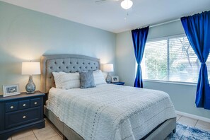 A bedroom with a bed, nightstands, a lamp, a vase, and curtains.