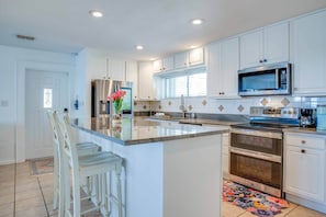 A modern kitchen with white cabinetry, a stainless steel refrigerator, a built-in microwave, and a gas stove.