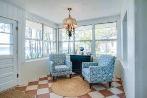 A sunroom with a checkered floor, two patterned armchairs, a globe, and a decorative lamp.