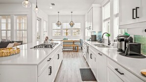Une cuisine moderne avec des meubles blancs, un îlot central et des luminaires suspendus.