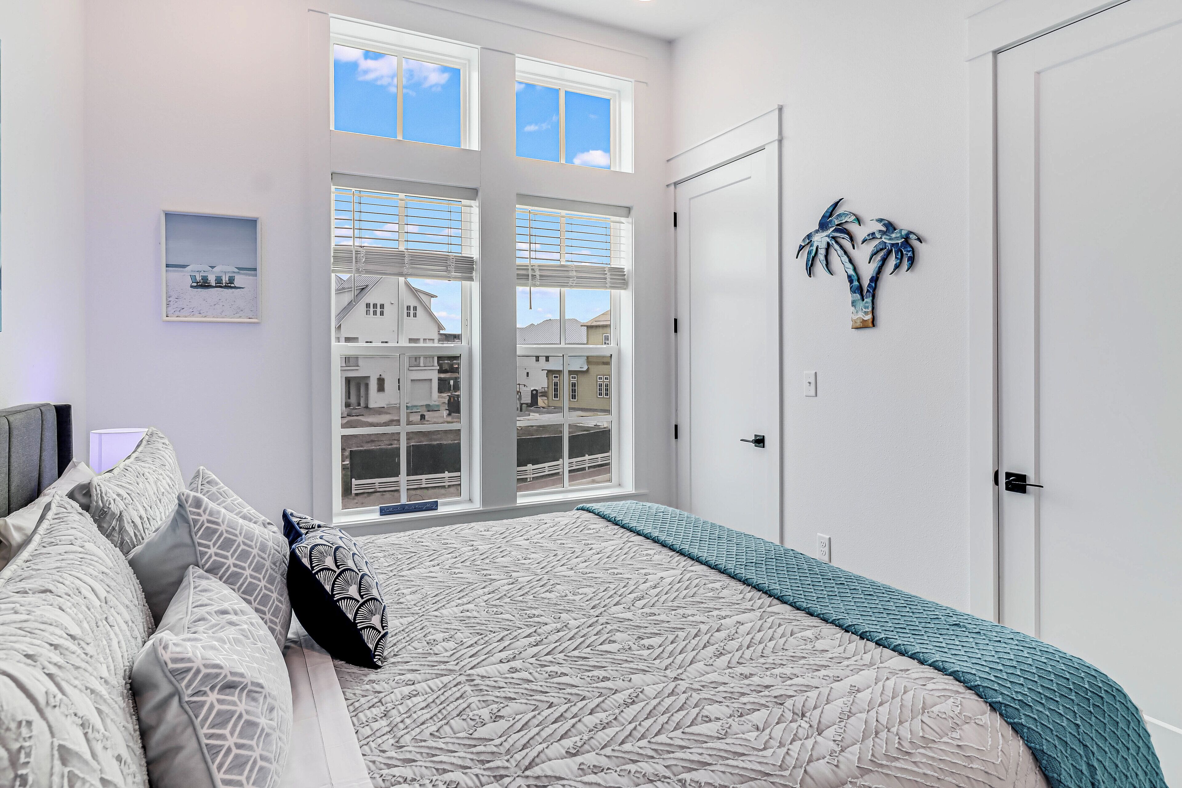 A bedroom with a large bed, a view of buildings through the window, and a door with a palm tree decoration.