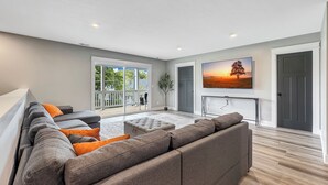 A modern living room with a large sectional sofa, a flat-screen TV mounted on the wall, and a sliding glass door leading to a balcony. - 6 BR, 4BA Franklin, IN Home (Franklin)