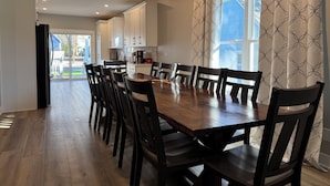 A dining area with a wooden table and chairs, a kitchen in the background, and a large window with patterned curtains. - 6 BR, 4BA Franklin, IN Home (Franklin)